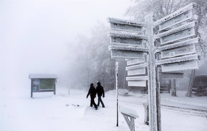 04 December 2020, North Rhine-Westphalia, Winterberg: Walkers walk by an icy signpost at the closed Kahler Asten ski area due to coronavirus (COVID-19) restrictions. Photo: Oliver Berg/dpa