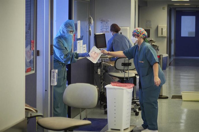 Una trabajadora sanitaria le da un material médico a una compañera para atender a un paciente de una habitación de la UCI de la Clínica Universidad de Navarra, en Pamplona