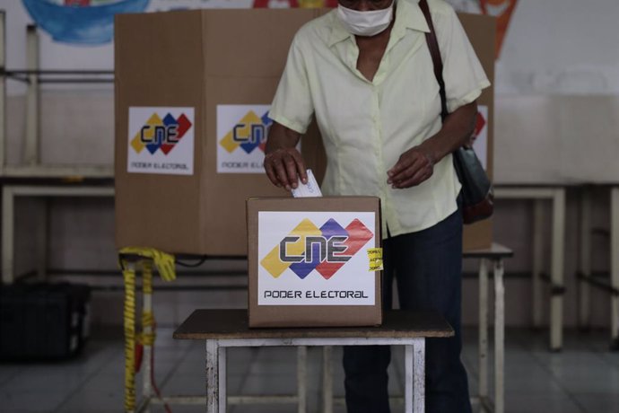 06 December 2020, Venezuela, Caracas: A woman casts her vote into a ballot box inside a polling station during the 2020 Venezuelan parliamentary election. Most opposition parties as well as interim president Guaido expect electoral fraud and have theref