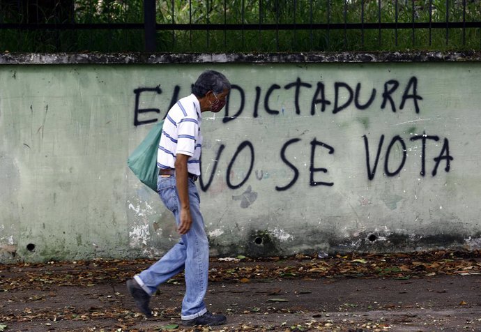 Un hombre pasea junto a un mural contra las elecciones parlamentarias de Venezuela