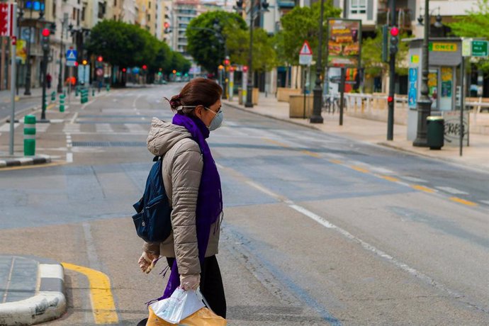 Una mujer protegida con mascarilla sanitaria camina por una de las calles desiertas de Valencia durante el Viernes Santo por el confinamiento impuesto por el Estado de Alarma provocado por el coronavirus, COVID19. En Madrid (España) a 10 de abril de 202