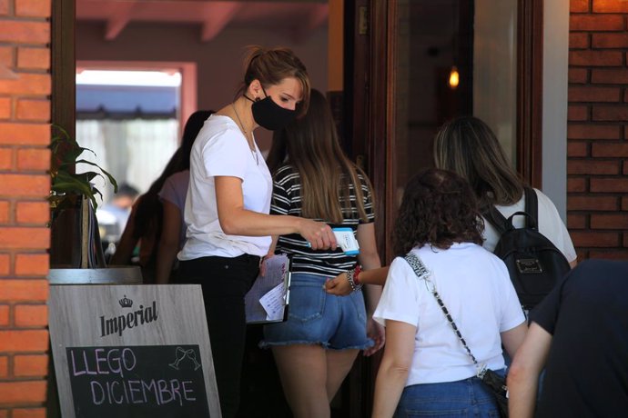 La trabajadora de un restaurante de Buenos Aires, toma la temperatura a sus clientes antes de su ingreso al establecimiento.