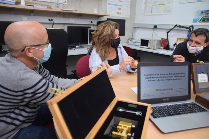 Imagen adjunta de Celia Gómez y los directores de su tesis, Fernando Quesada y Alejandro Melcón, observando los filtros de microondas para telecomunicaciones que ha desarrollado durante su investigación doctoral.