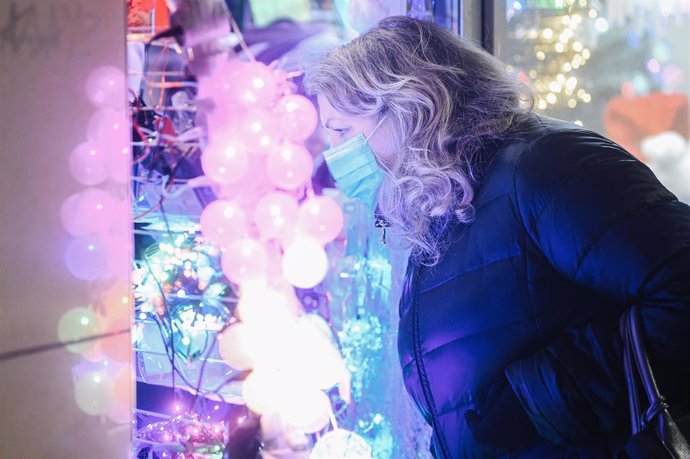 Una mujer con mascarilla mirando las lueces navideñas en una tienda