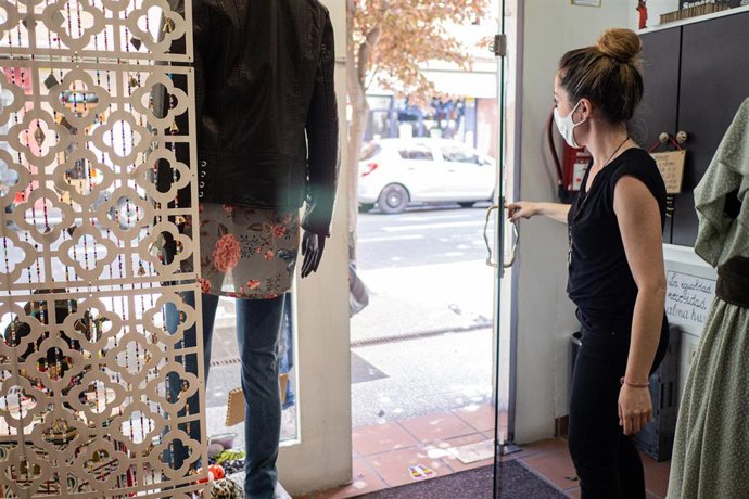 Una trabajadora desinfecta ropa colocada en un maniquí de su establecimiento.