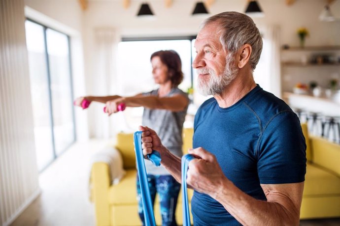 Pareja de personas mayores haciendo ejercicio en casa.