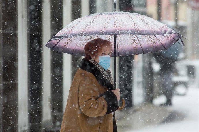 Una mujer se cubre de la nieve con un paraguas en Becerrea, en Lugo, Galicia (España), a 4 de diciembre de 2020. Hoy se ha producido la primera gran nevada del otoño en la montaña lucense. La intensa nevada que está cayendo sobre el centro de la provinc