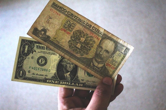 17 July 2020, Cuba, Havana: A man holds one Cuban peso and one US dollar as the Cuban government has abolished a ten percent tax on the purchase of US dollars due to lack of tourism revenue amid the coronavirus pandemic. Photo: Guillermo Nova/dpa