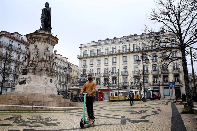 Un joven con mascarilla pasea en un patinete por Lisboa