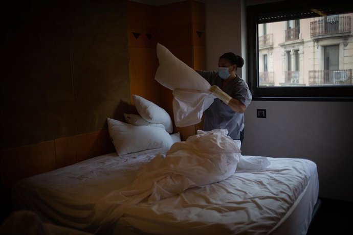 Una camarera de pisos cambia las sábanas de una cama de una habitación de hotel