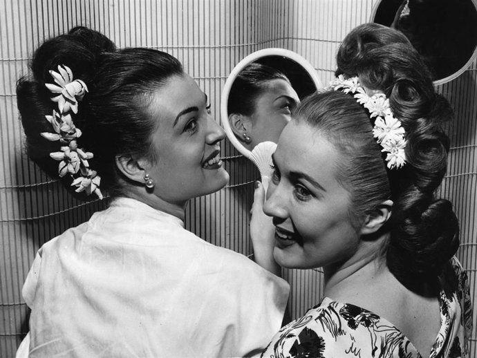 Two women admire their hairstyles in mirrors.