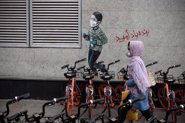 Una mujer pasa junto a un mural de un niño con mascarilla en Teherán, Irán
