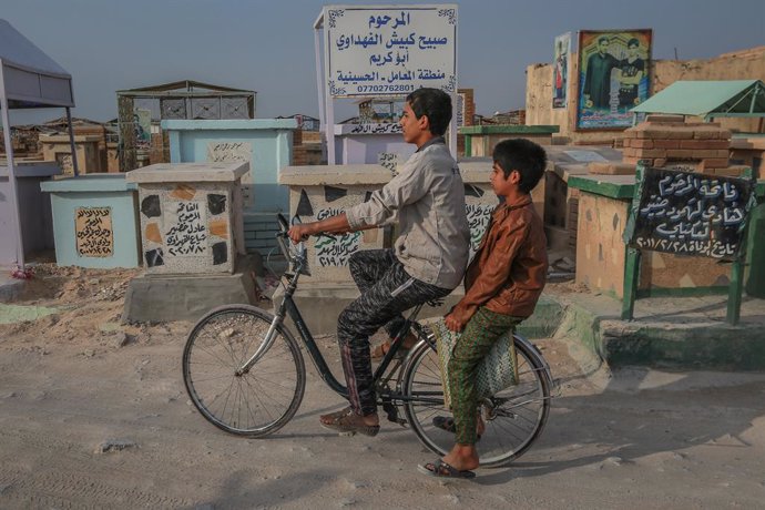 12 November 2020, Iraq, Najaf: Children ride a bicycle through Wadi al-Salam (Valley of Peace)cemetery in the Shiite holy city of Najaf. The ancient Islamic cemetery, established in 7th century near the shrine of Imam Ali, is  considered the world's la