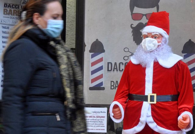 Una mujer con mascarilla pasando junto a un Papá Noel con mascarilla en Palermo, Sicilia, Italia