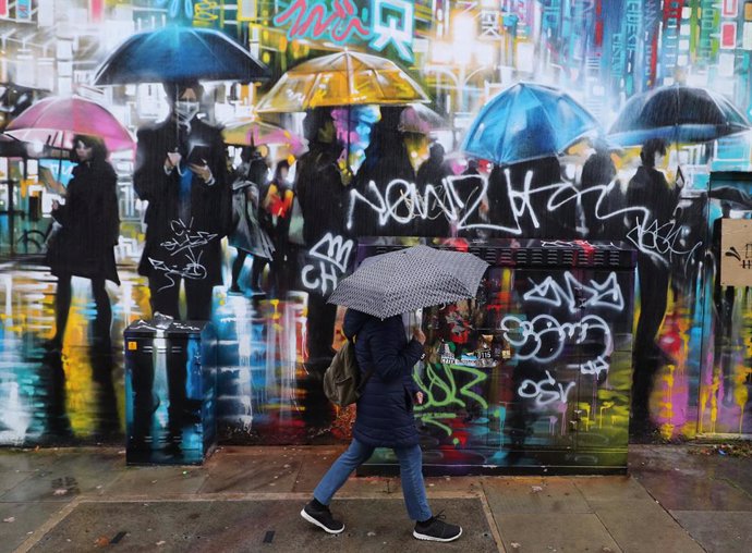 21 October 2020, England, London: A woman with an umbrella walks past a street mural. Photo: Yui Mok/PA Wire/dpa