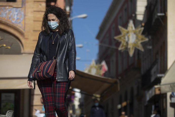 Una mujer con mascarilla camina por la plaza de San Francisco, al fondo las luces del alumbrado de navidad de la calle Sierpes, en Sevilla, foto de recurso