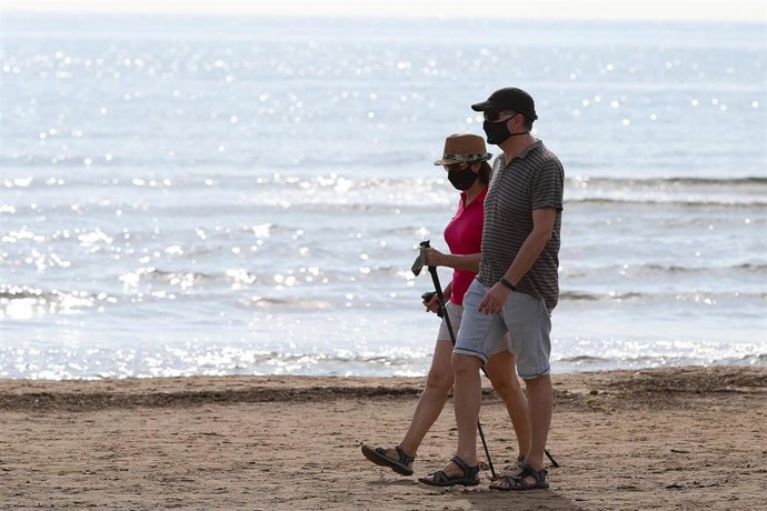 Dos personas protegidas con mascarilla pasean por la playa de la Malvarrosa