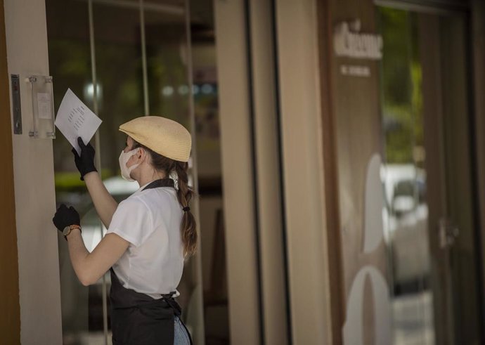 La empleada de una heladería colocando un cartel con el nuevo horario durante el tercer día de la fase 2 . En Sevilla, (Andalucía, España), a 27 de mayo de 2020.