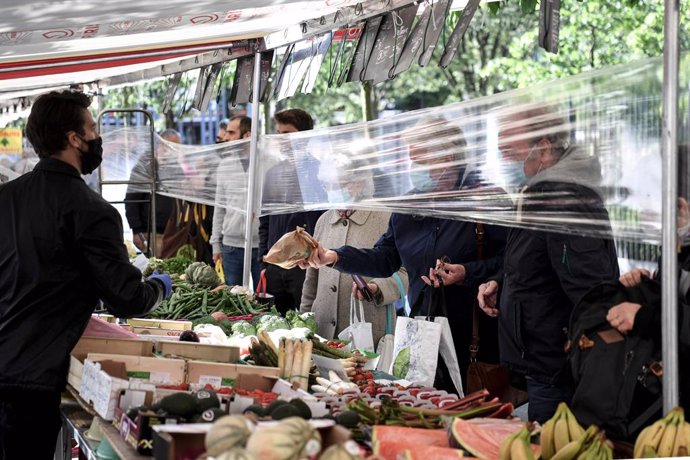 12 May 2020, France, Paris: A salesman wearing a face mask sells vegetables and fruit from behind a protective plastic sheet at "Place des Fetes" market. Photo: Alain Jocard/AFP/dpa