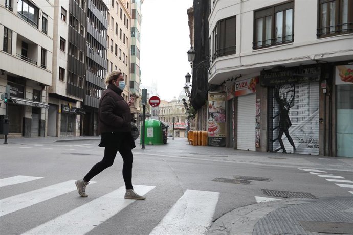 Una mujer protegida con una mascarilla camina por una calle vacía