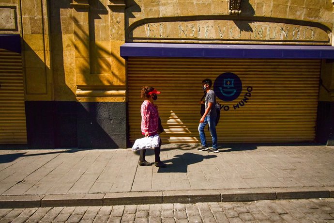19 December 2020, Mexico, Mexico City: People wearing face masks walk in front of a closed shop on Vicente Guerrero Street. Claudia Sheinbaum, the mayor of Mexico City announced that the metropolitan area that includes Mexico City and the State of Mexic