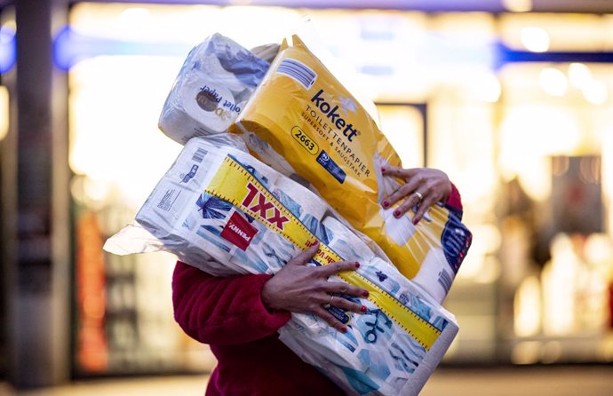 FILED - 05 November 2020, Hamburg: A woman walks out of a drug store with rolls of toilet paper during a wave of panic buying amid the coronavirus pandemic. Photo: Axel Heimken/dpa