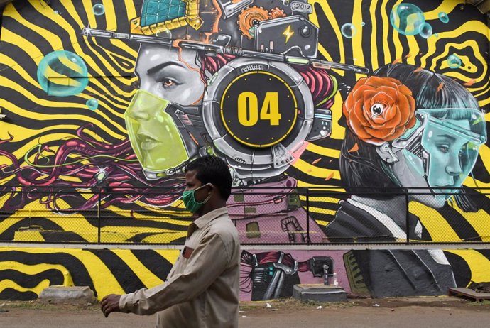 Un hombre con mascarilla pasa ante un mural en Bombay
