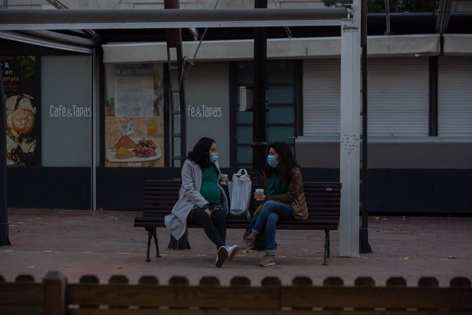 Dos mujeres charlan sentadas en un banco, en Barcelona, Catalunya (España), a 21 de diciembre de 2020. Debido al incremento de la curva de la pandemia en Catalunya y ante "la posible llegada de una tercera ola que incremente el nivel de presión sobre lo