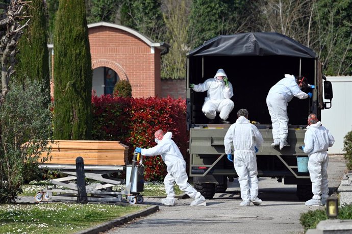 dpatop - 21 March 2020, Italy, Ferrara: People in protective suits transport a coffin with a corpse of the deceased due to the coronavirus in the cemetery of Ferrara. Military vans are having to transport coffins from Bergamo to other Italian cities, as