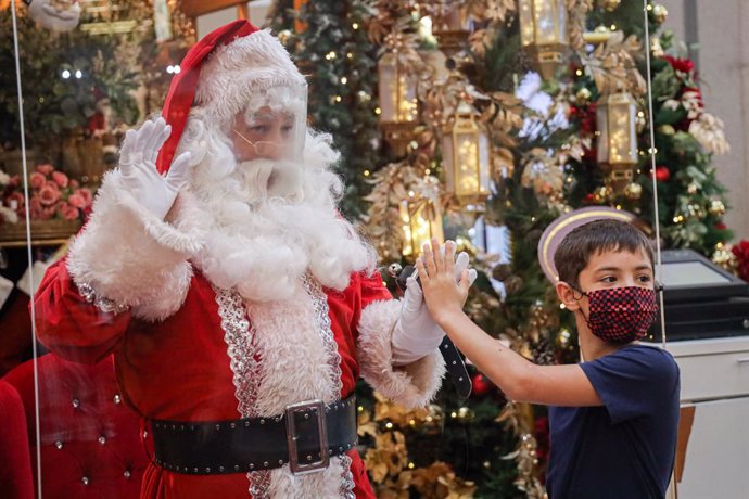 Un niño con mascarilla saluda a un Santa Claus con pantalla protectora en Kuala Lumpur