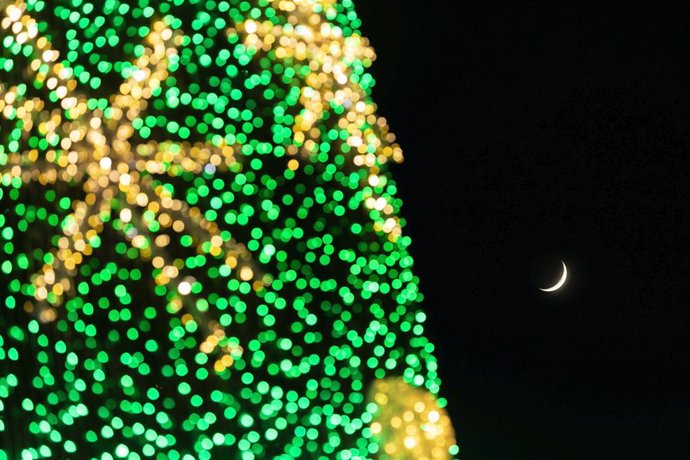 17 December 2020, Portugal, Lisbon: Crescent can be seen behind a Christmas tree, despite the coronavirus (COVID-19) pandemic, many people visit Terreiro do Paco to take photos of the Christmas tree. Photo: Hugo Amaral/SOPA Images via ZUMA Wire/dpa