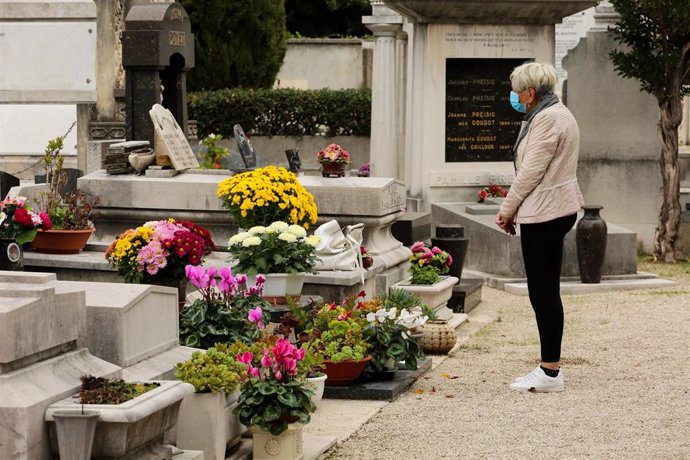 Una mujer con mascarilla frente a una tumba en un cementerio en Niza, Francia, durante la pandemia de COVID-19. 