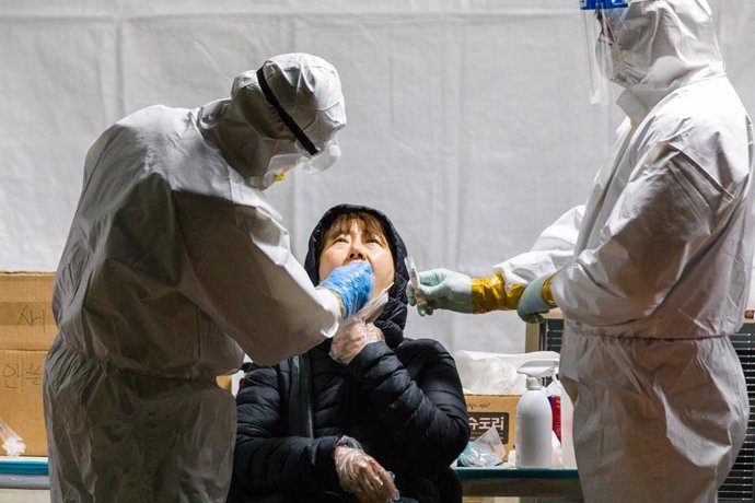 24 December 2020, South Korea, Seoul: Medical workers in protective suits take a throat swab for a coronavirus test from a woman at a temporary testing center at Sindorim metro station. Photo: Jintak Han/ZUMA Wire/dpa