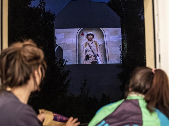 Mother and her daughter watch the movie projected on the backyard firewall of a residential building