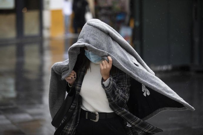 Una persona se protege de la lluvia con un abrigo. En Sevilla (Andalucía, España), a 04 de diciembre de 2020.