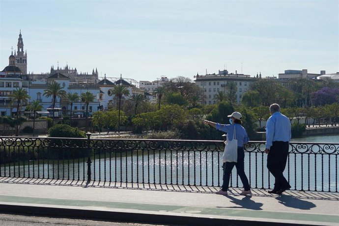 Personas mayor protegido con mascarilla pasea por el puente de Triana.