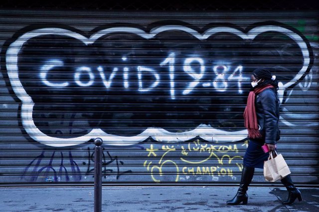 Una mujer con mascarilla frente a una persiana con una pintada de la COVID-19 en París, Francia