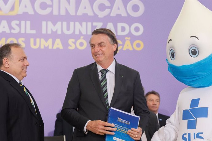 HANDOUT - 16 December 2020, Brazil, Brasilia: Brazilian President Jair Bolsonaro poses for a photo with the mascot Ze Gotinha, a traditional character in Brazil created to raise awareness about the coronavirus vaccines, during the launch of the National