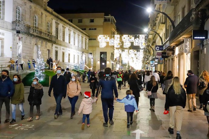 Transeúntes pasean bajo las luces navideñas, llevando mascarilla, alguno con gorro navideño, en Vigo, Galicia (España), a 25 de diciembre de 2020