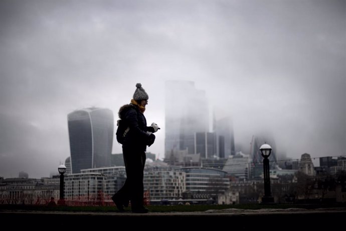 28 December 2020, England, London: A woman walk past a view of the City of London which is covered in low mist. Photo: Victoria Jones/PA Wire/dpa