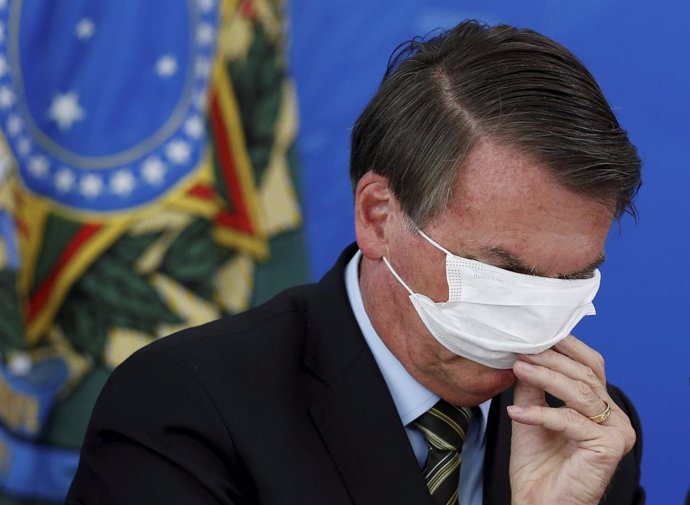 El presidente de Brasil, Jair Bolsonaro, intenta ponerse una mascarilla.