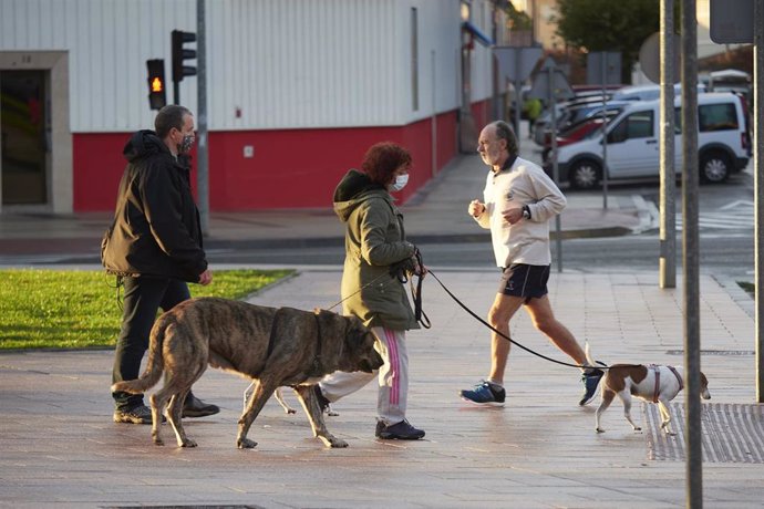 Una persona pasea a sus dos mascotas mientras un corredor se cruza a su paso por una céntrica calle de Pamplona, Navarra (España), a 13 de octubre de 2020. Hoy entran en vigor nuevas medidas restrictivas en Navarra ante el incremento de casos de Covid-1