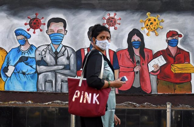 Una mujer con mascarilla pasa ante un mural con trabajadores con mascarilla en Bombay