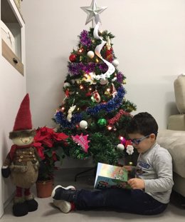 Fotografía de recurso de un niño leyendo un libro junto al árbol de Navidad