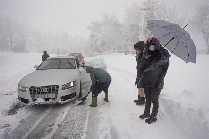 Varias personas limpian la carretera con una pala para ayudar a un coche atrapado en la nieve en Pedrafita do Cebreiro, en Lugo, Galicia (España), a 29 de diciembre de 2020. El temporal de nieve ha dificultado la circulación en más de un centenar de car