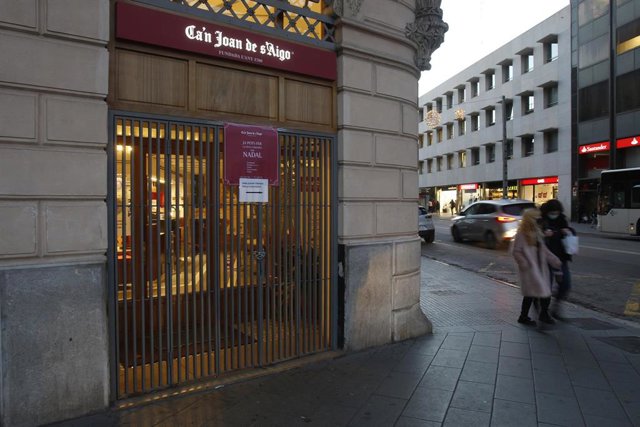 Dos viandantes pasan por delante de una cafetería en Palma, Mallorca (España), a 29 de diciembre de 2020, donde el cierre se ha adelantado 
