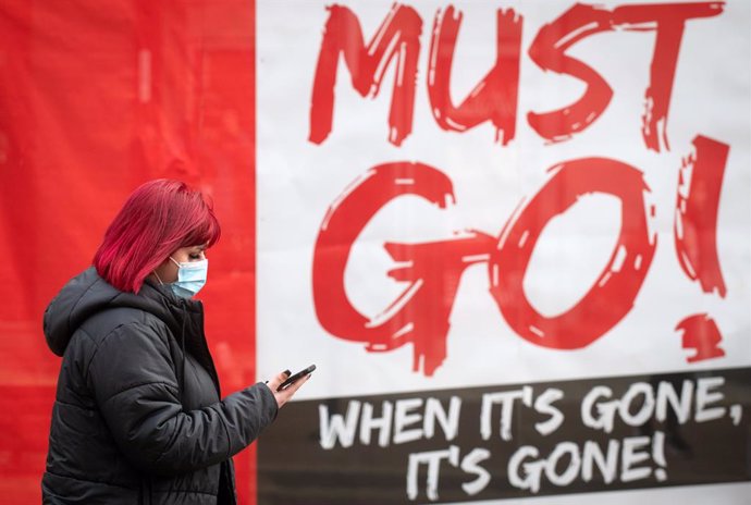 30 December 2020, England, Northampton: A woman wearing a face mask walks past a sign in a shop window, as further changes to England's tier system are expected to be announced, just days after millions of people came under harsher coronavirus restricti