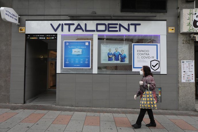Una mujer con mascarilla pasa junto a la entrada de una clínica Vitaldent el día en el que la empresa ha reabierto su red de clínicas en todo el territorio nacional, entre ellas las 47 de la región madrileña, tras implementar un protocolo post Covid-19 