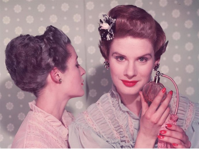 A Woman With Bright Red Nail Varnish Sprays Herself With Perfume Using An Atomiser