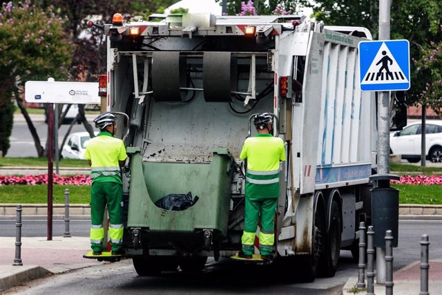 Dos trabajadores del servicio de recogida de basuras, vacian un contenedor en el camión.